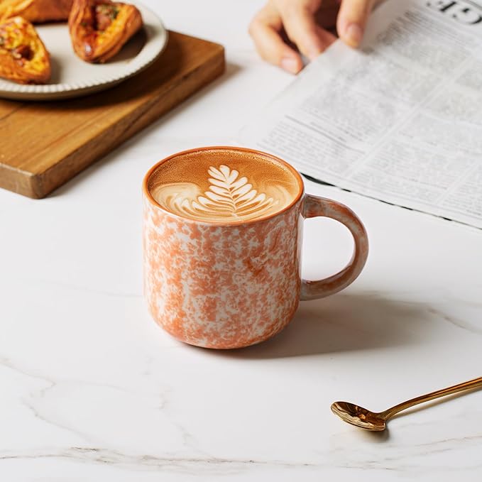 Speckled ceramic coffee mug with handle, orange exterior with latte art on top