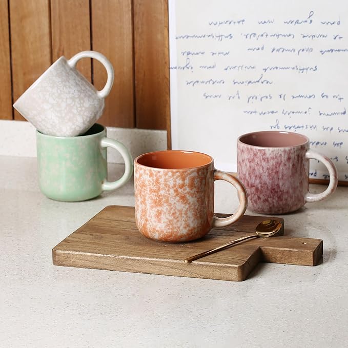 Assorted ceramic coffee mugs with handles on a wooden board, pastel green and orange tones