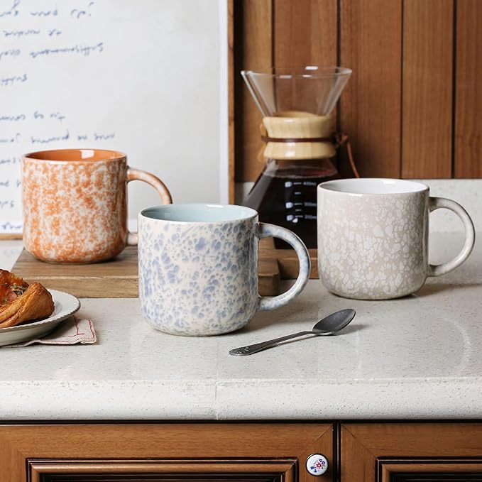 Set of ceramic coffee mugs with handles on a tabletop, including speckled blue and white