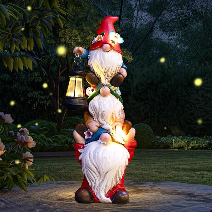 Triple outdoor garden gnome statue with red hat and warm glowing solar lantern on grass