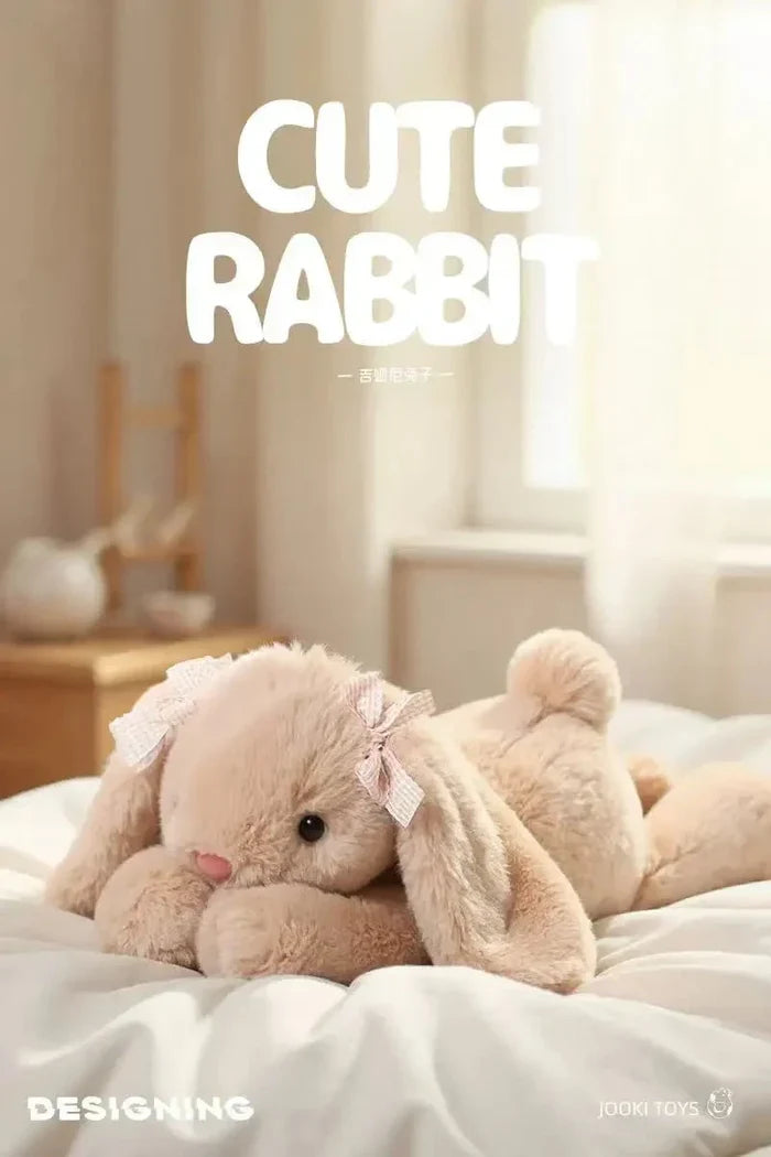 Beige plush rabbit toy pillow, ribbon bow detail on one ear, reclining on soft fabric.