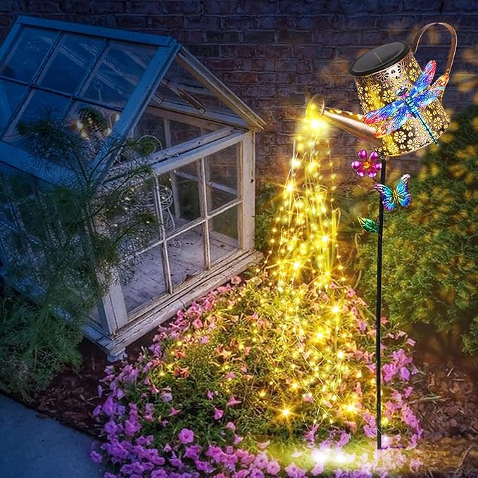 Solar watering can stake lights with dragonfly decorations, warm yellow glow by flower bed