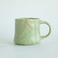 Mint green ceramic coffee mug with abstract red and white accents, curved handle