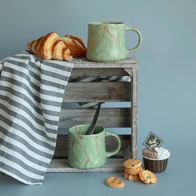 Mint green ceramic coffee mugs set with red and white abstract design, on wooden shelf