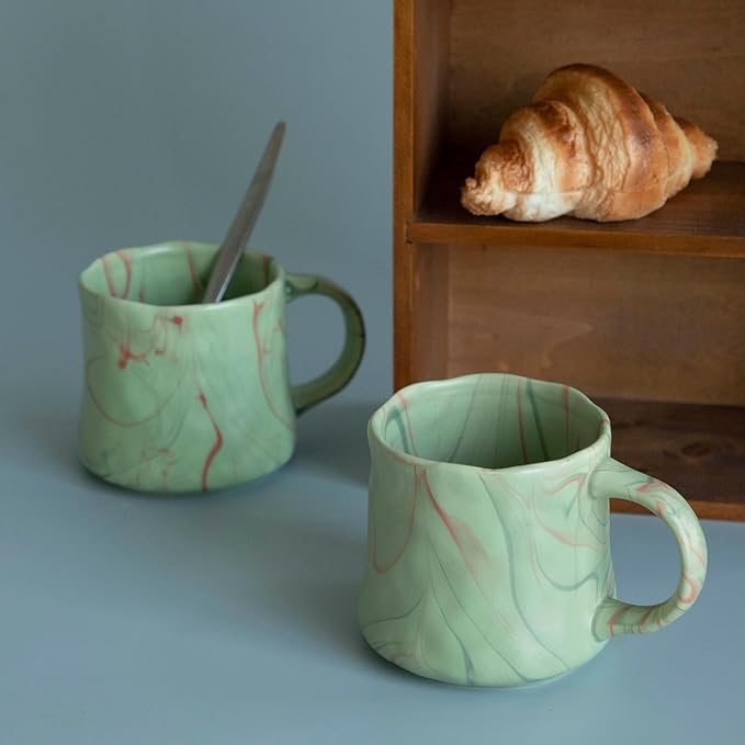 Mint green ceramic coffee mugs set with red and white abstract patterns, angled view