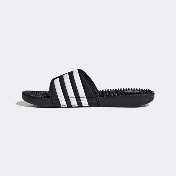 Adidas Adissage Slide sandals in black with white stripes and textured massage footbed, side view.