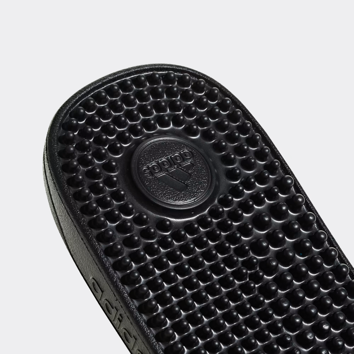 Adidas Adissage Slide sandals footbed in black featuring textured massaging nubs and debossed Adidas logo detail, close-up view.