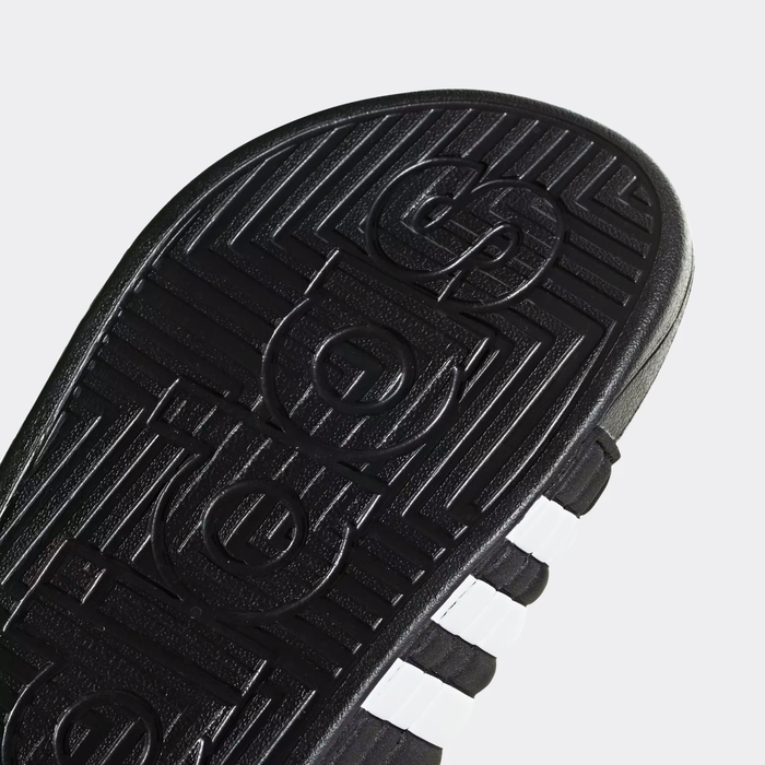 Adidas Adissage Slide sole view with black textured rubber featuring Adidas branding, white side stripes, and durable construction.