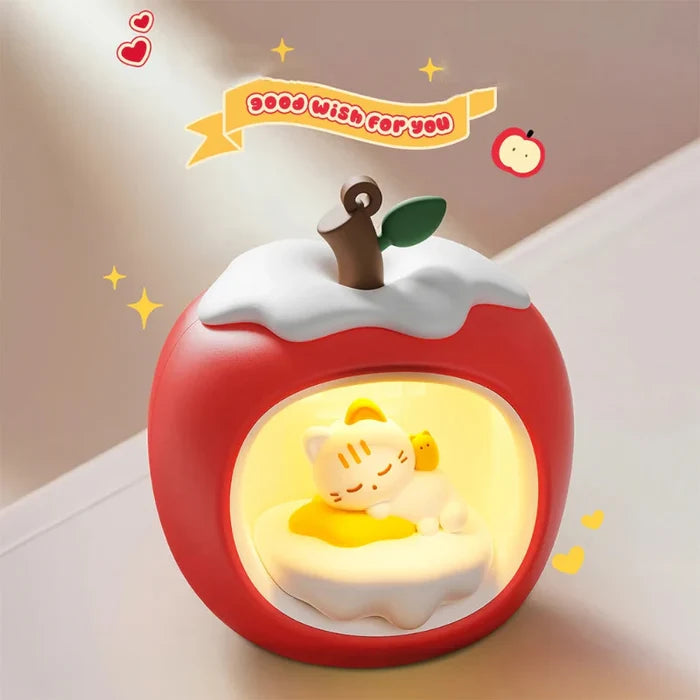 Red apple-shaped night light with white cloud top and glowing window showing sleeping cat.