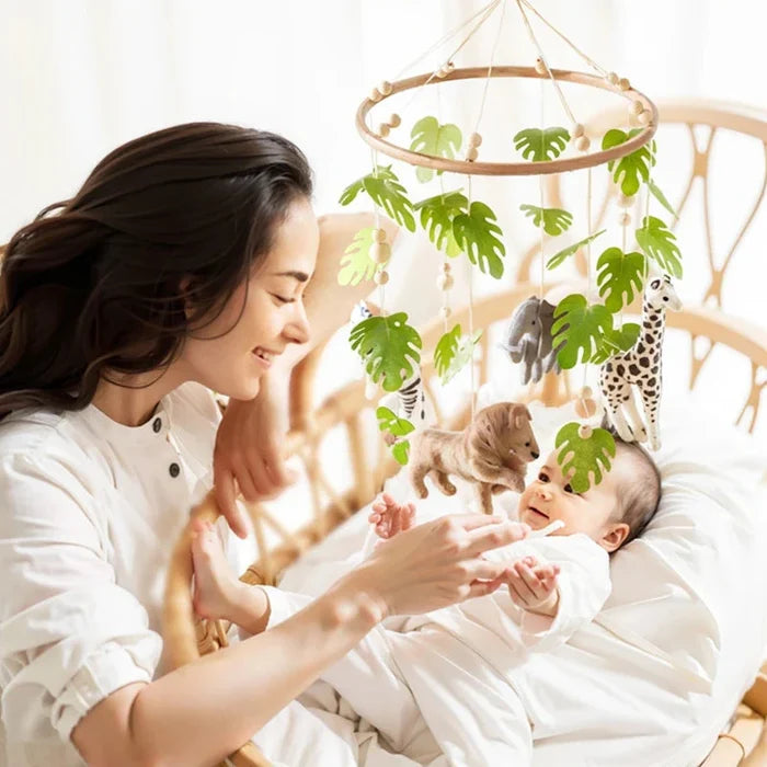 Baby crib mobile with hanging forest animal and leaf plush toys near a parent