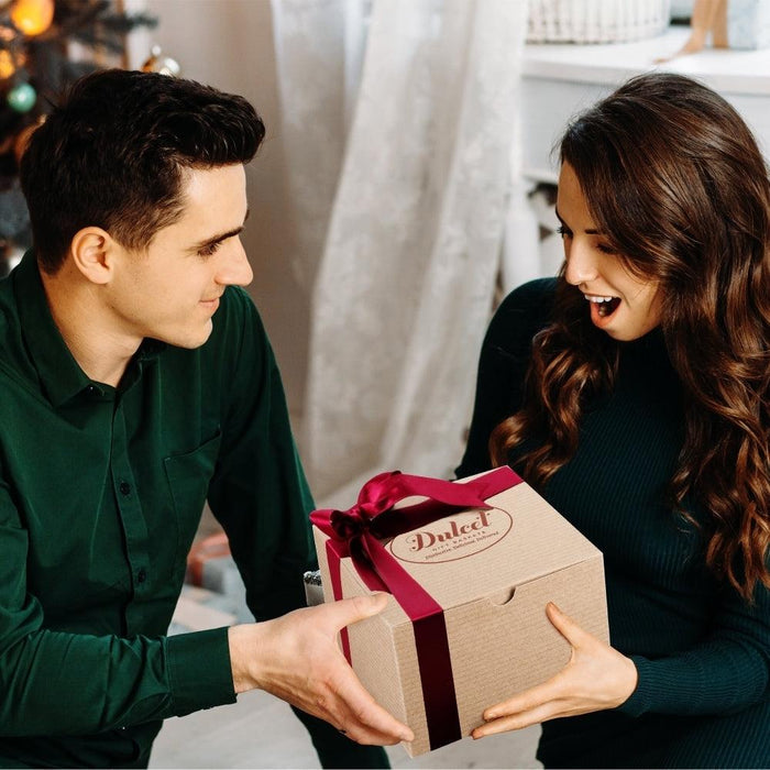 Dulcet gift box with ribbon held by two people in a cozy room.