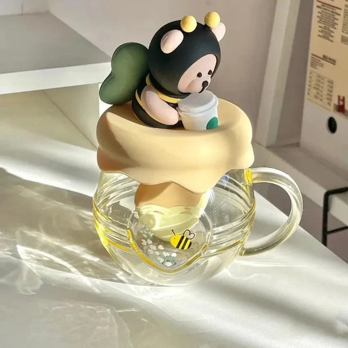 Glass tea infuser mug with bear infuser figure and honey-yellow lid, visible honeybee art