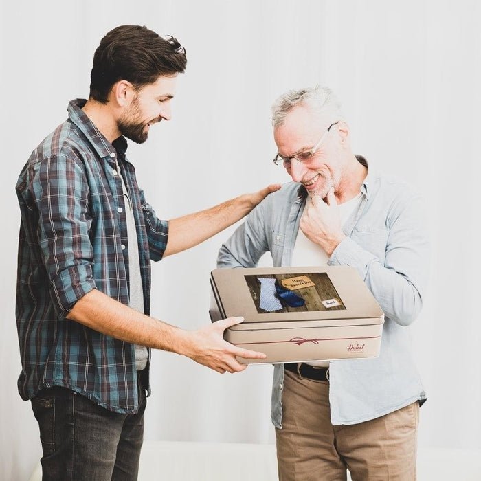Man presenting a gift tin to an older man, with ribbon detail on the box