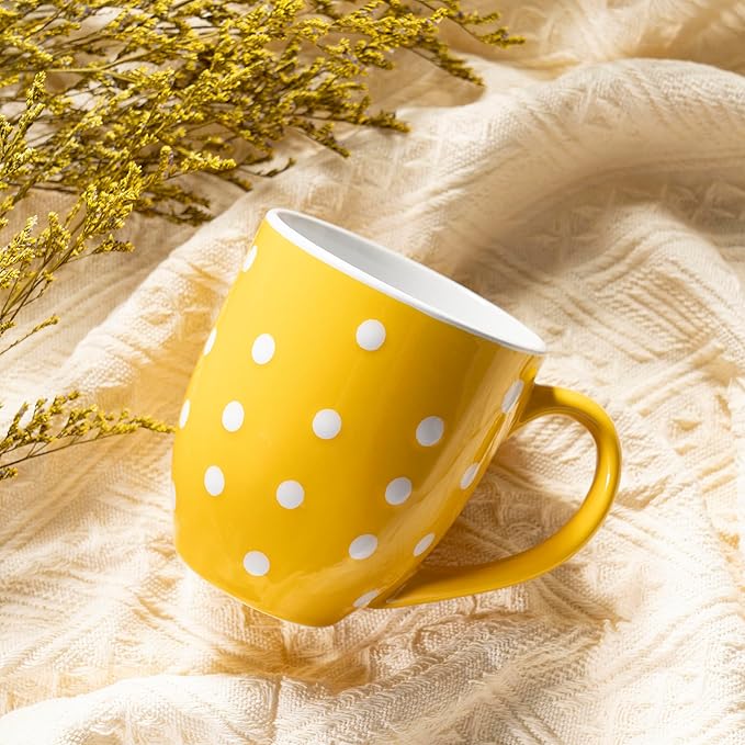 Yellow ceramic coffee mug with white polka dots and side handle on light fabric.