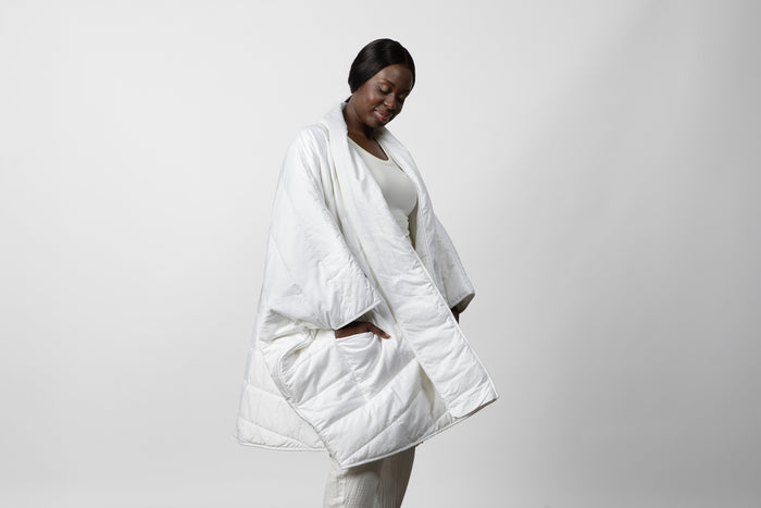 A woman wearing a white Blanket Robe with hands in side pockets, standing against a light background