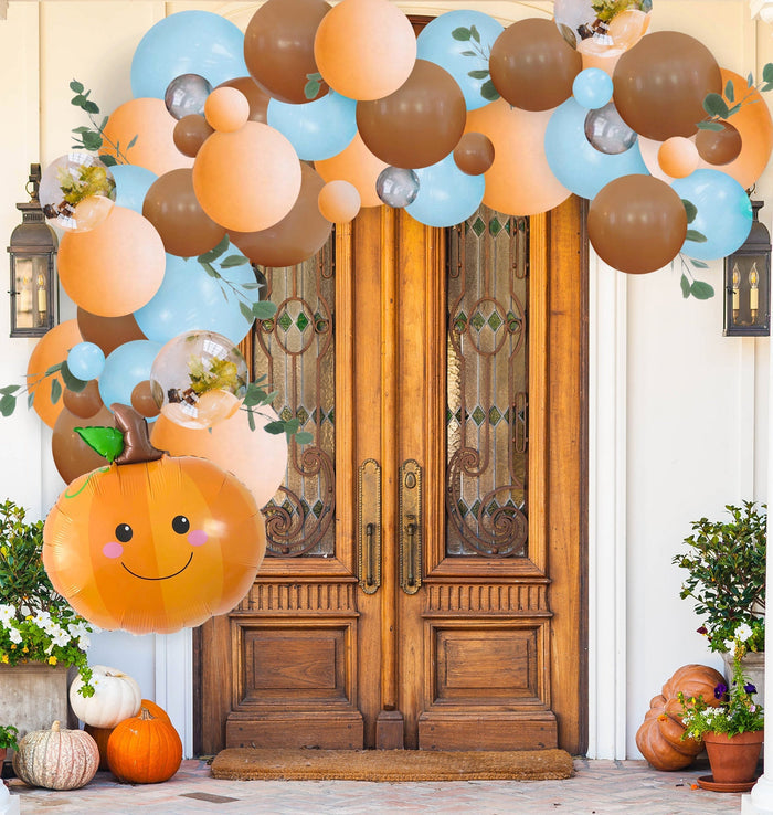 Pumpkin face balloon with orange garland of pastel blue and brown balloons and leaves