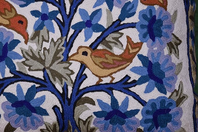Blue and white embroidered pillow cover detail with birds, blossoms, and leafy branches.