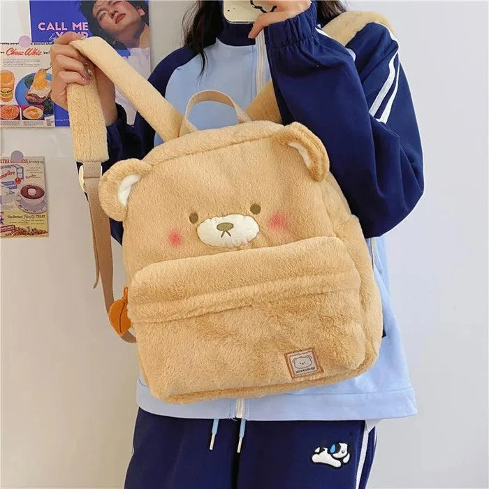 Light tan plush bear backpack worn, featuring bear face patch and rectangular front label