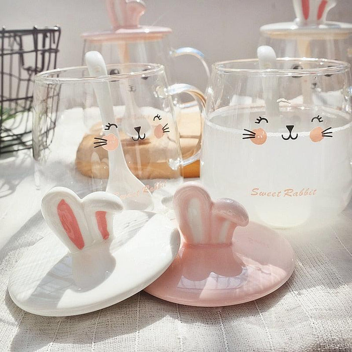 Two glass bunny mugs with bunny-ear lids, bunny face print, and matching spoon rest