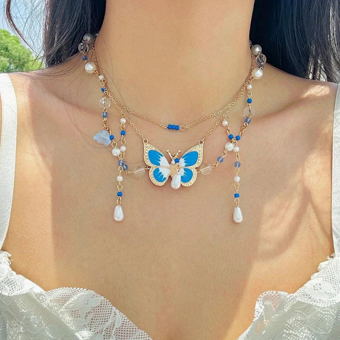 Gold multi-layer pearl necklace with blue butterfly pendant, white faux pearls, and blue drops