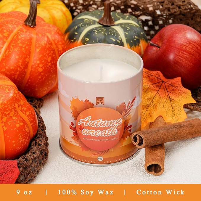 White autumn wreath candle jar on white surface with cinnamon sticks and pumpkins around