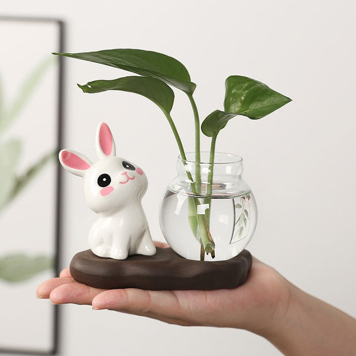 Ceramic bunny planter with a clear glass vase holding green stems on a dark base