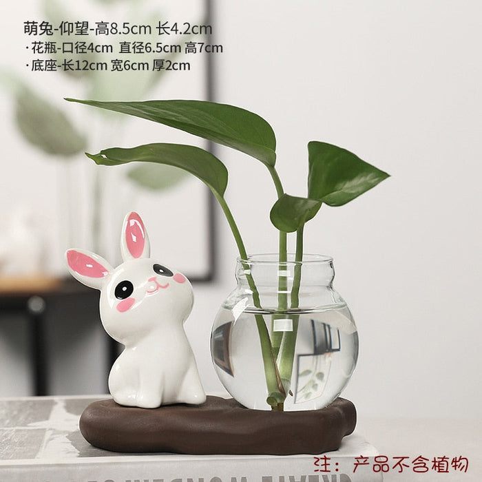 Ceramic bunny planter with clear glass vase and tall green leaves on dark oval base