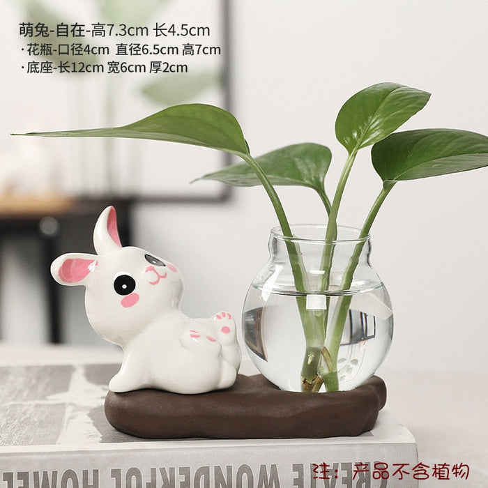 Ceramic bunny planter with clear glass vase of green stems, small bunny figure on base