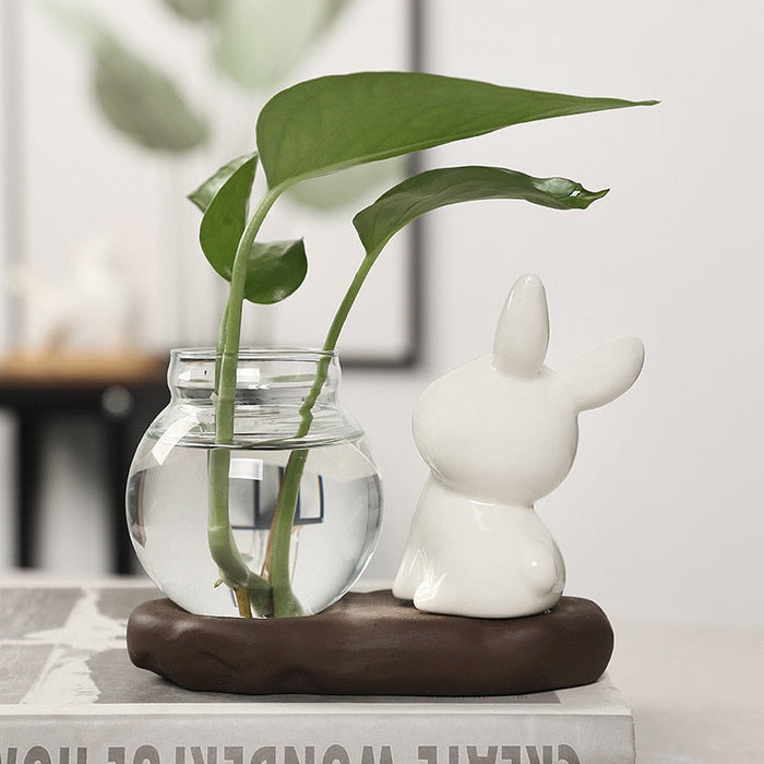Ceramic bunny planter with clear glass vase and one large green leaf, bunny on dark base