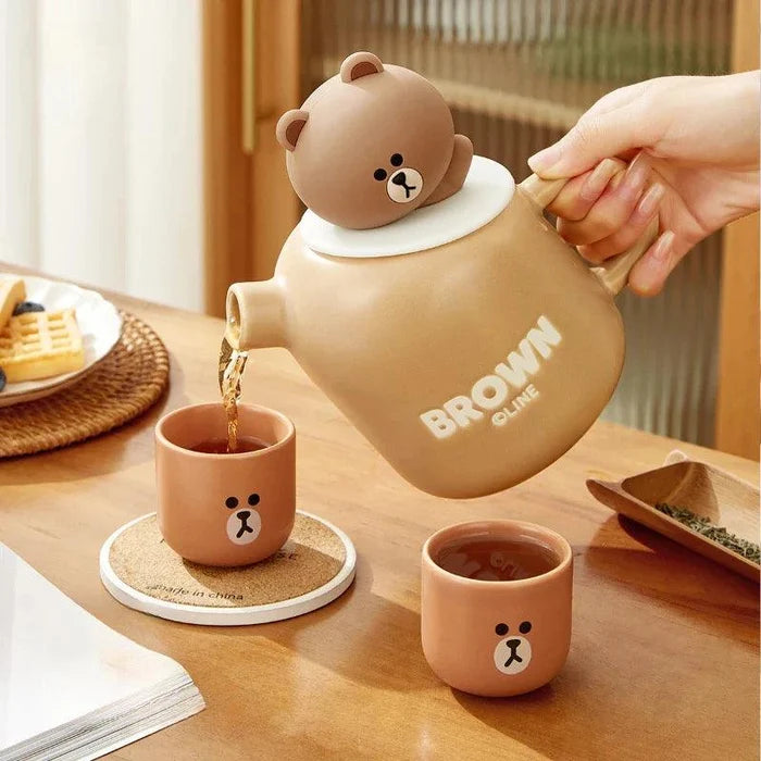 Ceramic teddy bear teapot with lid and brown cups, pouring spout and bear face emblem.