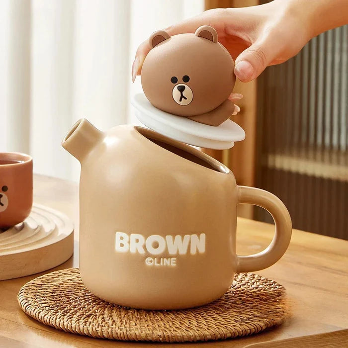 Ceramic teddy bear teapot with round lid topper, bear face emblem, and handle on coaster.