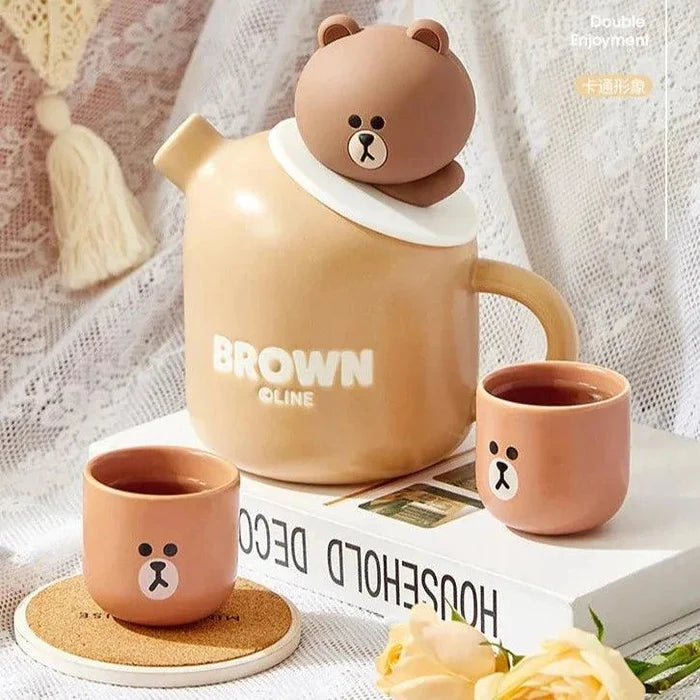 Ceramic teddy bear teapot with two brown cups and bear-face logo, round lid topper.