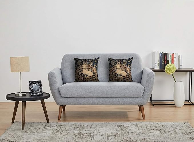 Set of two navy tapestry pillow covers with tan unicorn scenes on a sofa