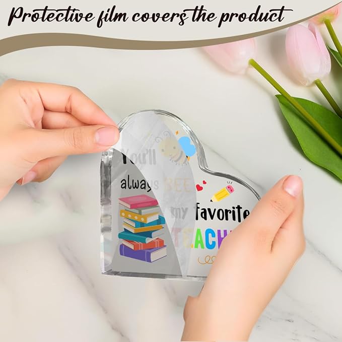 Hands remove protective film from clear acrylic heart teacher gift with bee artwork.