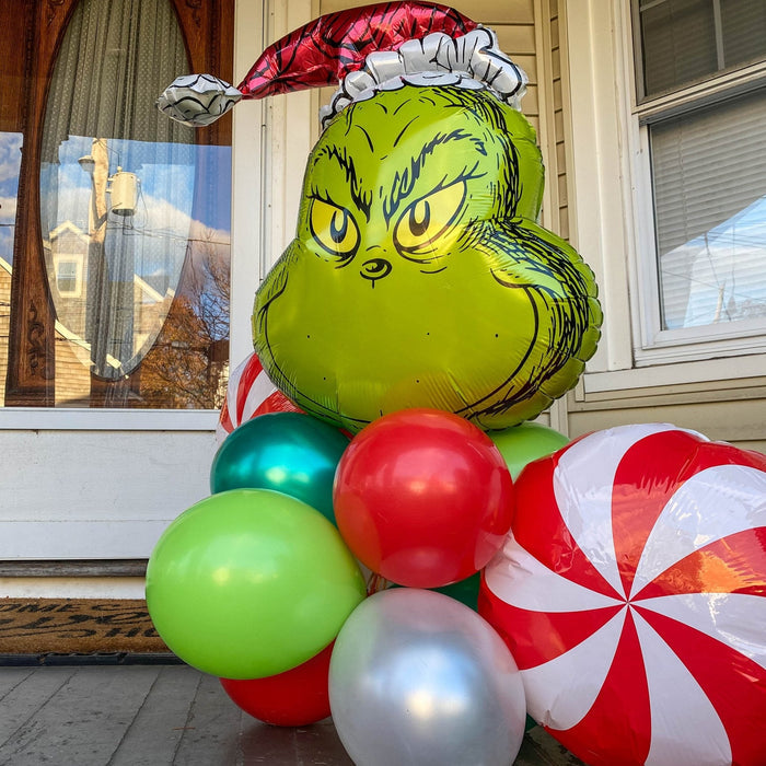 Grinch-themed balloon bouquet featuring green Grinch face balloon and red peppermint balloon arcs