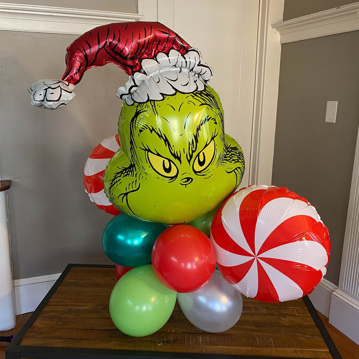 Grinch balloon bouquet on a table with green face balloon, red-and-white peppermint balloons