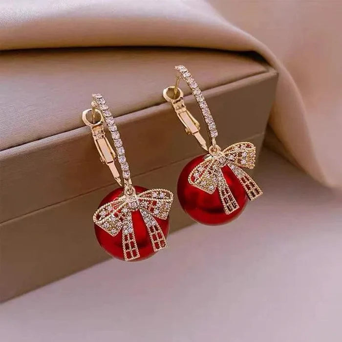 Ornament-style drop earrings with red round charms, rhinestone bows, and gold-tone hoops