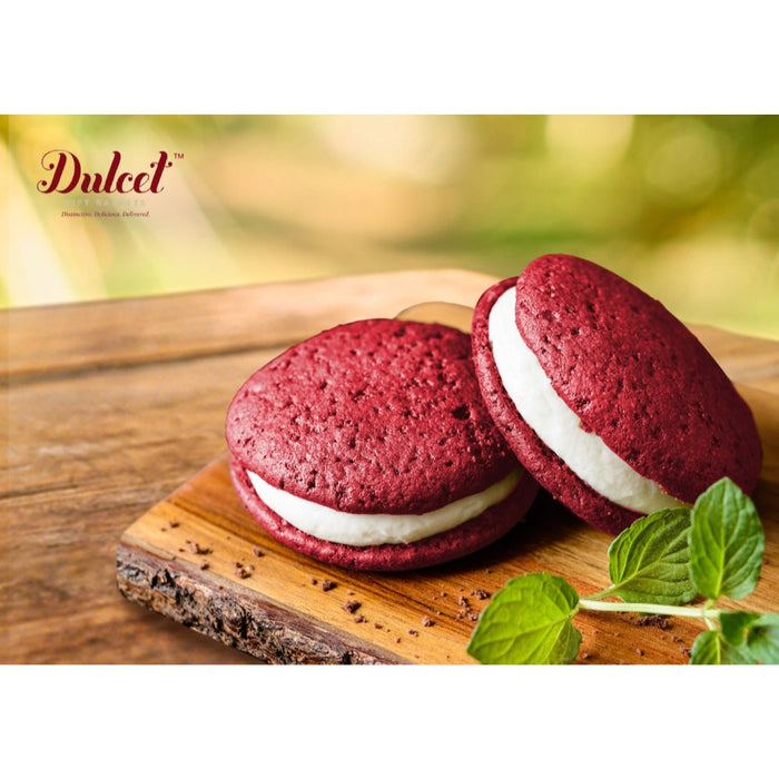 Red sandwich cookies with white filling on wooden board, garnished with mint leaves
