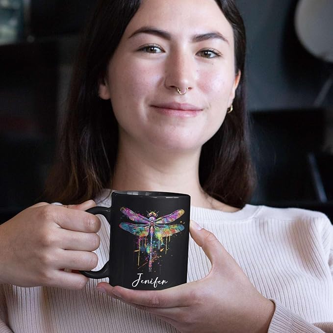Black ceramic mug with colorful dragonfly graphic and custom name, held in hand