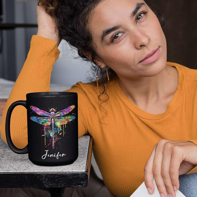 Black ceramic coffee mug with colorful dragonfly graphic and custom name on tabletop