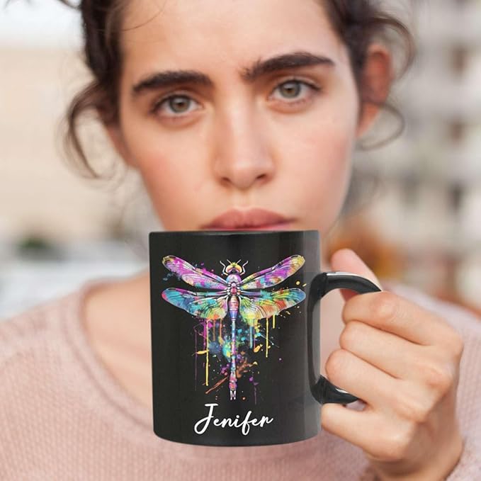 Black ceramic mug with colorful dragonfly graphic and custom name, held for a sip