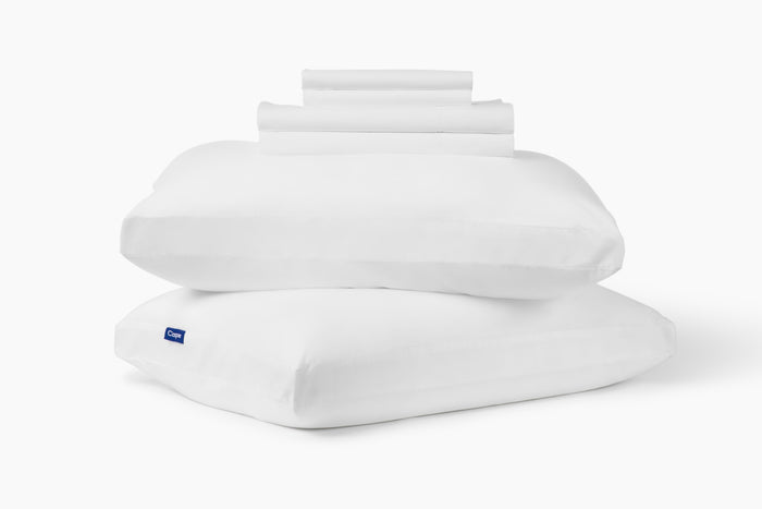 White pillowcase, folded, stacked on top of two pillows against a white background