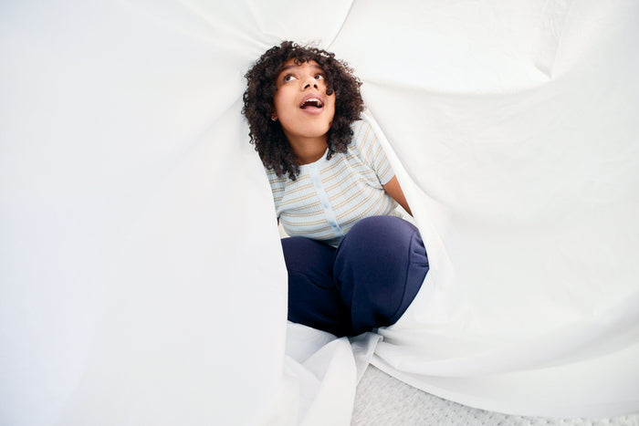 Child sitting inside a white sheets on a bed