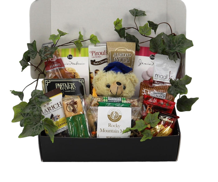 Black gift box filled with packaged snacks, plush bear, and green vines.