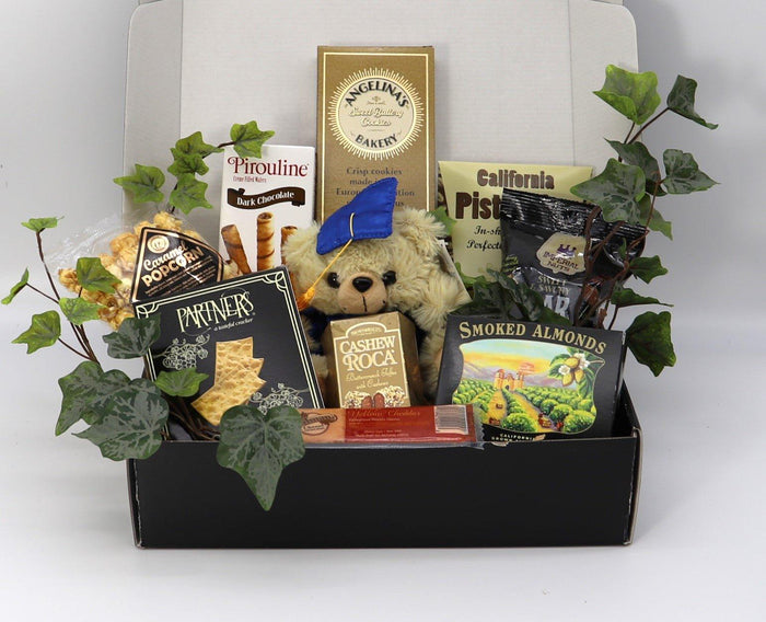 Black gift box with plush bear and assorted snack packages, surrounded by leaves.
