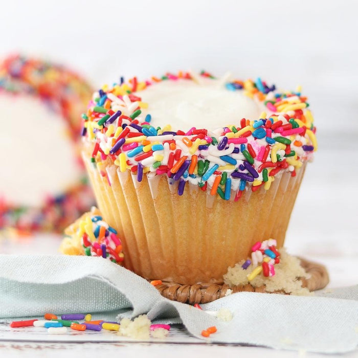 Rainbow-sprinkle cupcake with golden paper liner and white frosting on a tray