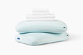 White sheet set, folded, stacked on top of two Hybrid Snow Pillows against a white background