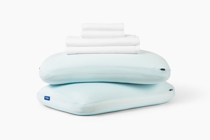 White sheet set, folded, stacked on top of two Hybrid Snow Pillows against a white background