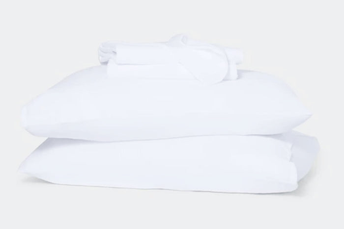 Stack of white sheet set, folded, on top of two pillows against a white background