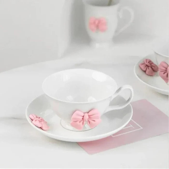 White tea cup with pink bow ornament on saucer, heart-shaped handles